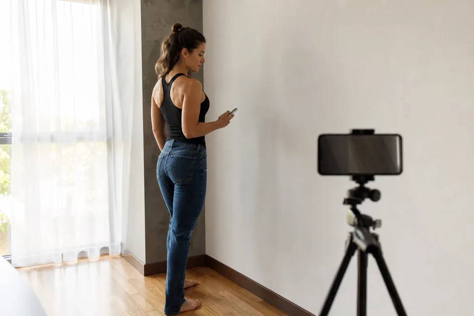 Smartphone on a tripod facing a white wall by a window, set up to shoot model digitals at home